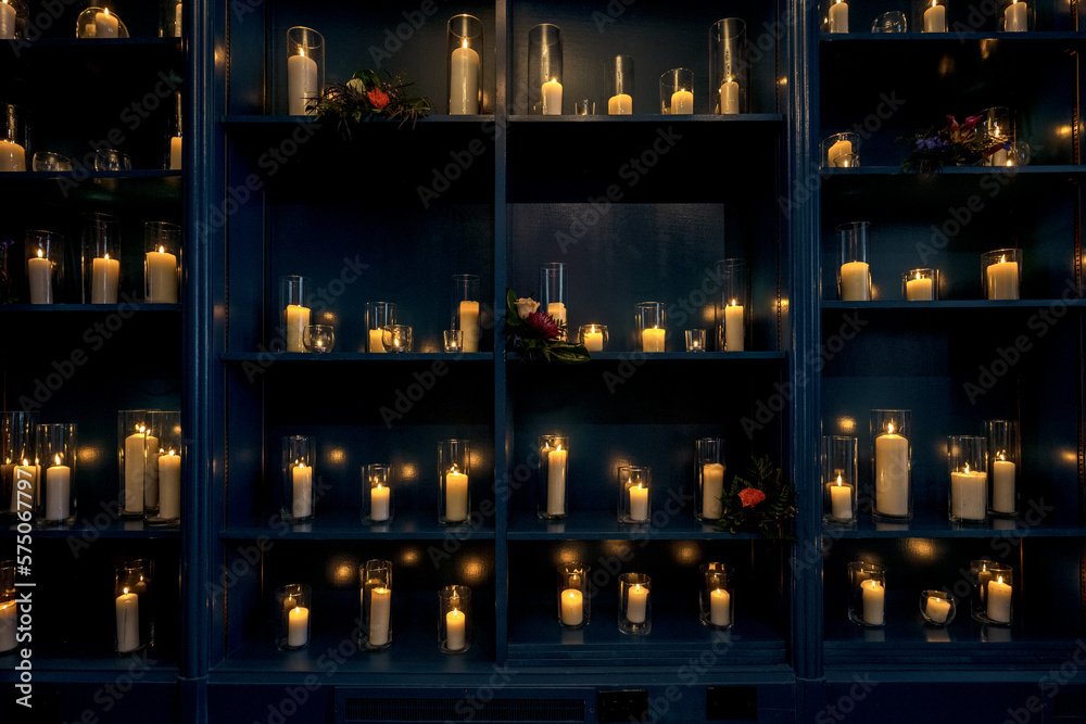 Blue Bookcase wall full of white candles with fire burning