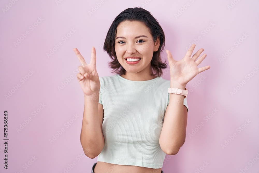 Hispanic young woman standing over pink background showing and pointing up with fingers number seven while smiling confident and happy.