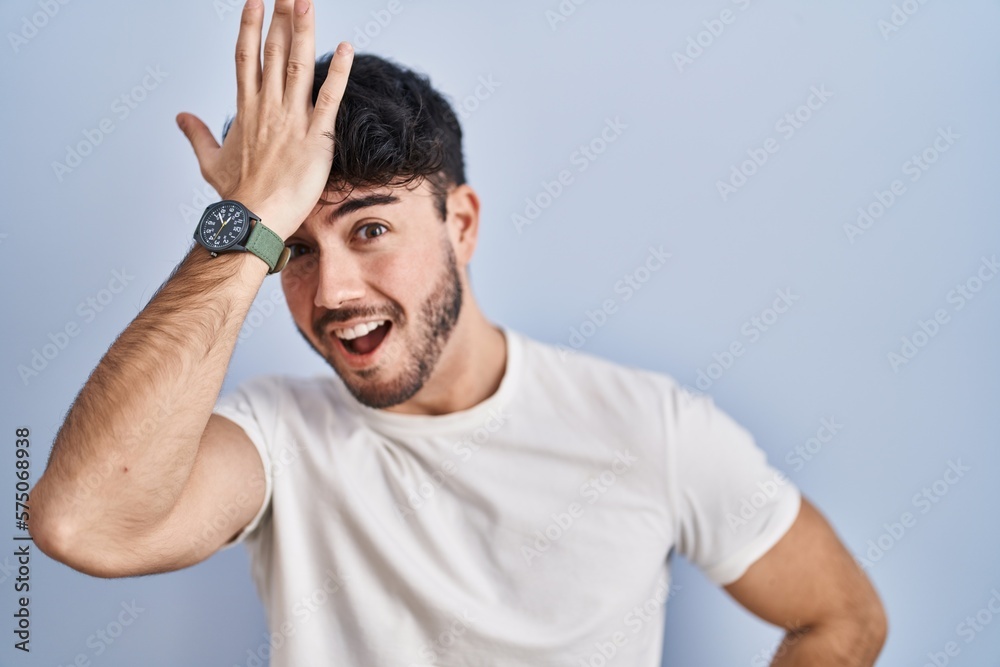 Fototapeta premium Hispanic man with beard standing over white background surprised with hand on head for mistake, remember error. forgot, bad memory concept.