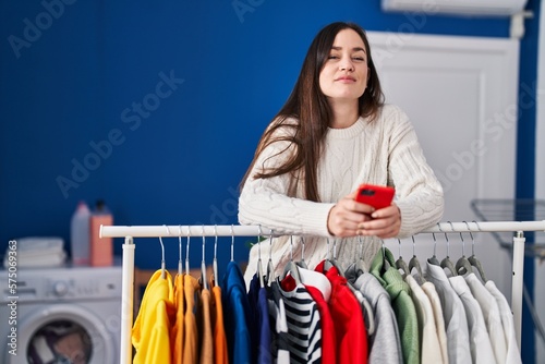 Young brunette woman waiting for laundry using smartphone relaxed with serious expression on face. simple and natural looking at the camera.