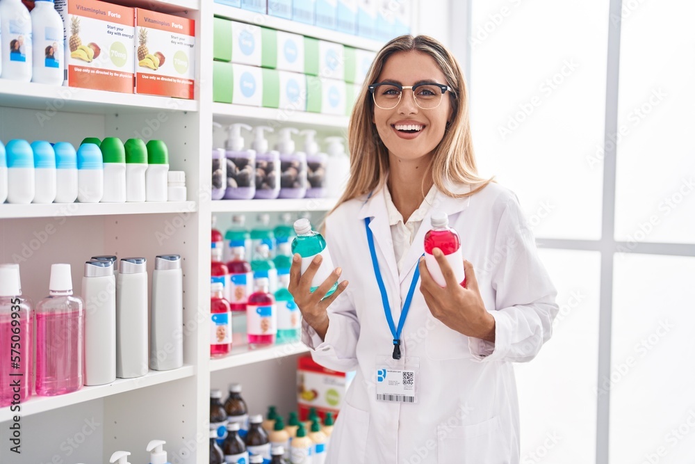 Young blonde woman pharmacist smiling confident holding medication bottles at pharmacy