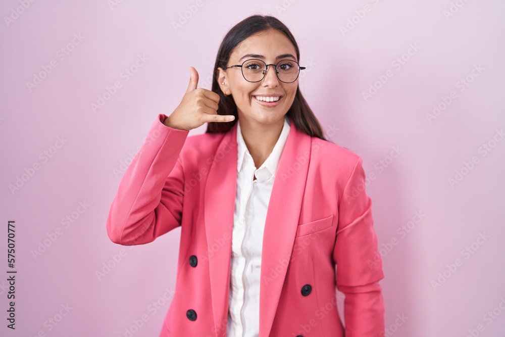 Young hispanic woman wearing business clothes and glasses smiling doing phone gesture with hand and fingers like talking on the telephone. communicating concepts. Young hispanic woman wearing business clothes and glasses smiling doing phone gesture with hand and fingers like talking on the telephone. communicating concepts.