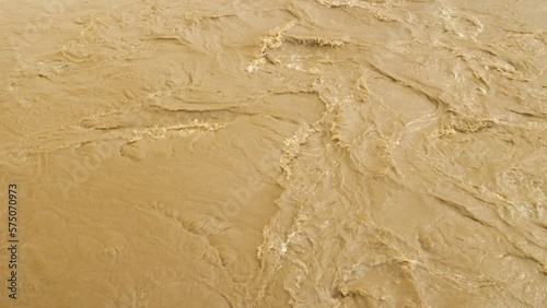 A top view of the swift muddy gurgling water in the river. Flooding. A weather disaster. Natural disasters. Brown river carrying rubbish. Extreme weather photo