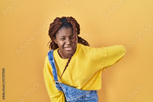 African woman standing over yellow background suffering of backache, touching back with hand, muscular pain © Krakenimages.com