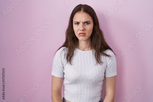 Young hispanic girl standing over pink background skeptic and nervous, frowning upset because of problem. negative person.