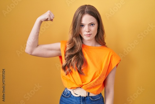 Caucasian woman standing over yellow background strong person showing arm muscle, confident and proud of power