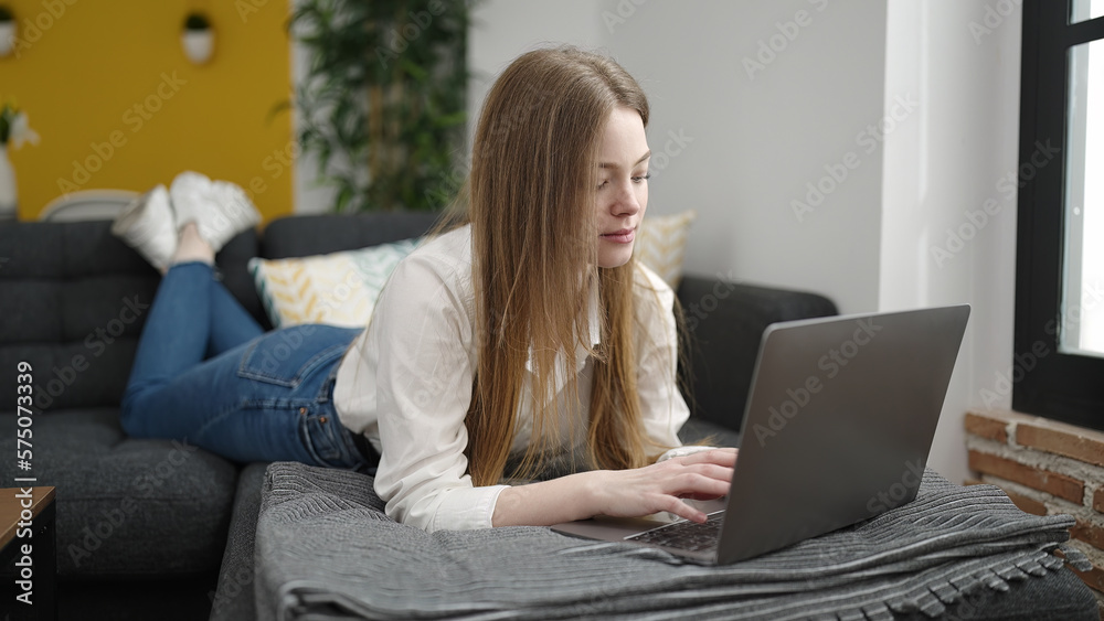 Young blonde woman using laptop lying on sofa at home Young blonde woman using laptop lying on sofa at home