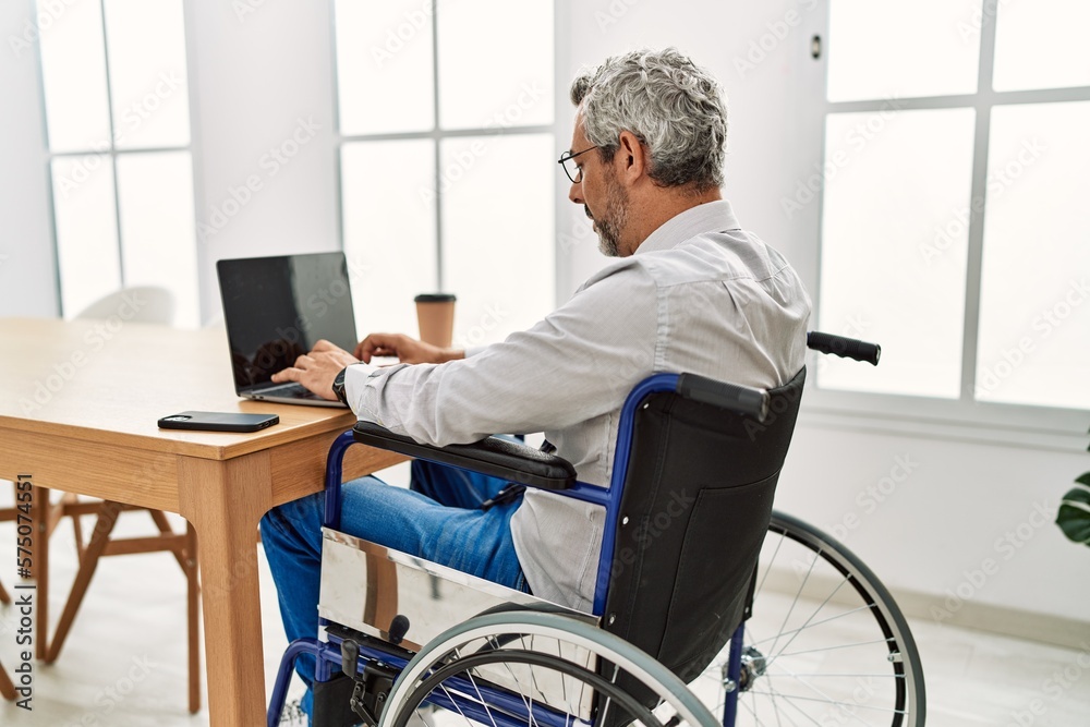 Middle age grey-haired man business worker sitting on wheelchair working at office