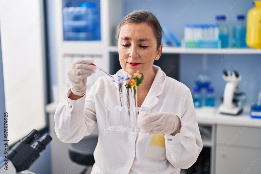Middle age woman scientist pouring liquid on flower at laboratory Middle age woman scientist pouring liquid on flower at laboratory