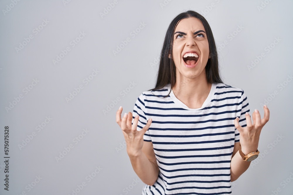 Young brunette woman wearing striped t shirt crazy and mad shouting and yelling with aggressive expression and arms raised. frustration concept. Young brunette woman wearing striped t shirt crazy and mad shouting and yelling with aggressive expression and arms raised. frustration concept.