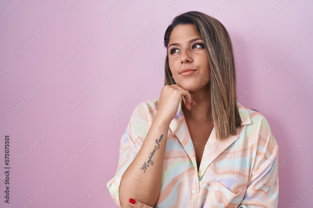 Blonde woman standing over pink background with hand on chin thinking about question, pensive expression. smiling with thoughtful face. doubt concept. Blonde woman standing over pink background with hand on chin thinking about question, pensive expression. smiling with thoughtful face. doubt concept.