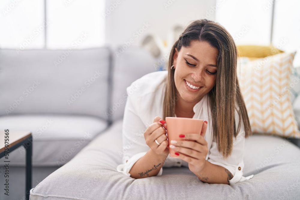 Young hispanic woman drinking coffee lying on sofa at home Young hispanic woman drinking coffee lying on sofa at home