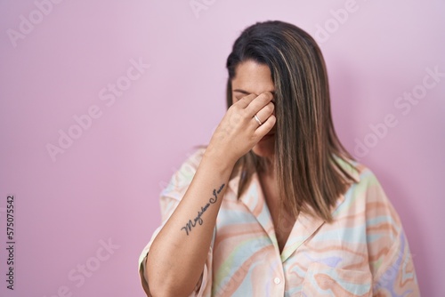 Blonde woman standing over pink background tired rubbing nose and eyes feeling fatigue and headache. stress and frustration concept.