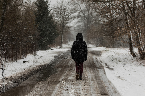 walking person in black jacket on the country road on a sad snowy winter day