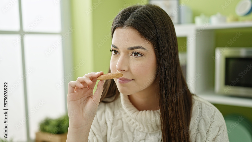 Young beautiful hispanic woman smelling cookie sitting on table at home Young beautiful hispanic woman smelling cookie sitting on table at home