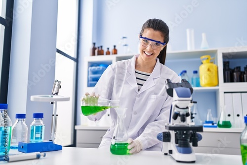 Fototapeta Naklejka Na Ścianę i Meble -  Young beautiful hispanic woman scientist pouring liquid on test tube at laboratory