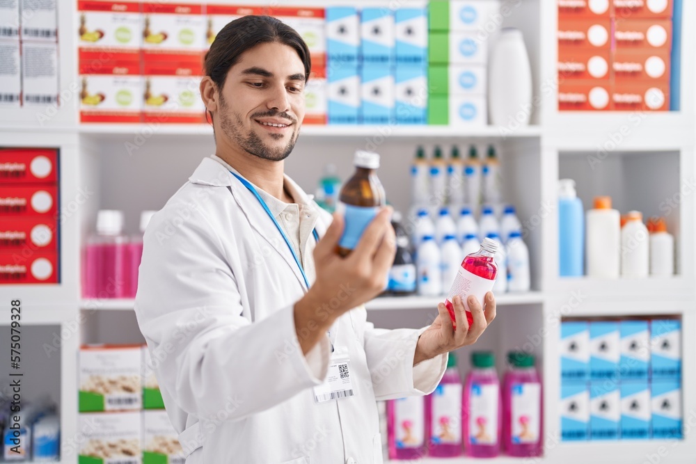 Young hispanic man pharmacist smiling confident holding medication bottles at pharmacy