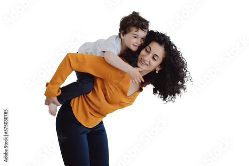 Playful curly Italian boy riding on mom against transparent background. Hispanic woman babysitter rolling up on back cheerful kid at home. Caucasian sister entertains brother. Childhood, maternity