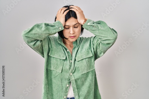 Young asian woman standing over white background suffering from headache desperate and stressed because pain and migraine. hands on head.