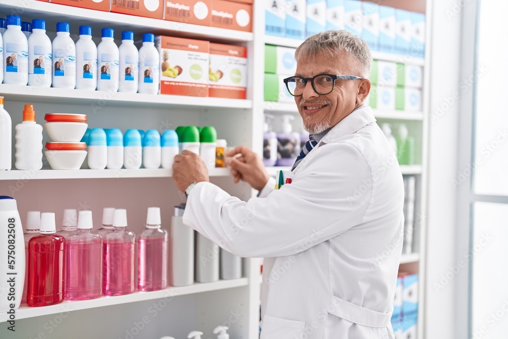 Middle age grey-haired man pharmacist holding deodorant bottle at laboratory