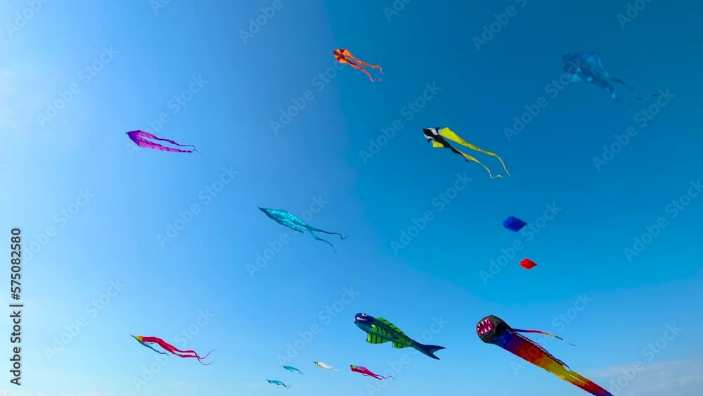 Many different colorful kites are flying in the blue sky and swaying in the wind during summer outdoor festival. Childhood, freedom and leisure time concept