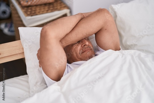 Middle age grey-haired man stressed lying on bed at bedroom