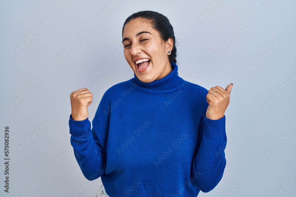 Young hispanic woman standing over isolated background very happy and excited doing winner gesture with arms raised, smiling and screaming for success. celebration concept. Young hispanic woman standing over isolated background very happy and excited doing winner gesture with arms raised, smiling and screaming for success. celebration concept.