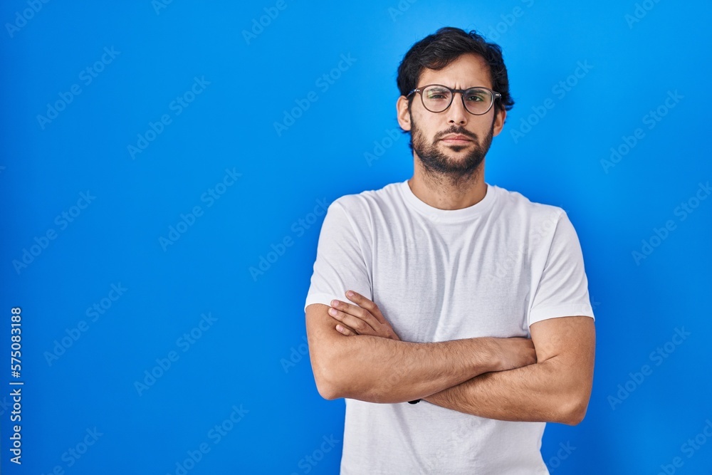 Handsome latin man standing over blue background skeptic and nervous, disapproving expression on face with crossed arms. negative person. Handsome latin man standing over blue background skeptic and nervous, disapproving expression on face with crossed arms. negative person.