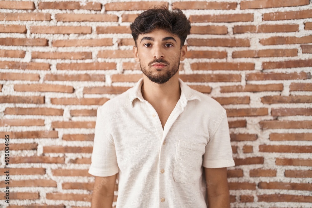 Arab man with beard standing over bricks wall background relaxed with serious expression on face. simple and natural looking at the camera. Arab man with beard standing over bricks wall background relaxed with serious expression on face. simple and natural looking at the camera.