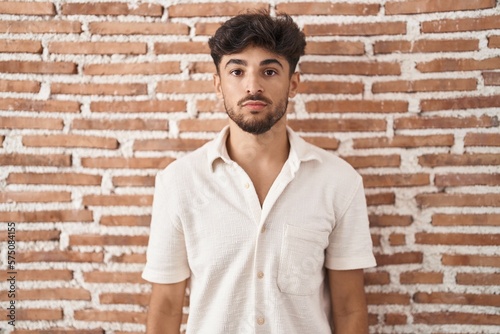 Arab man with beard standing over bricks wall background relaxed with serious expression on face. simple and natural looking at the camera.