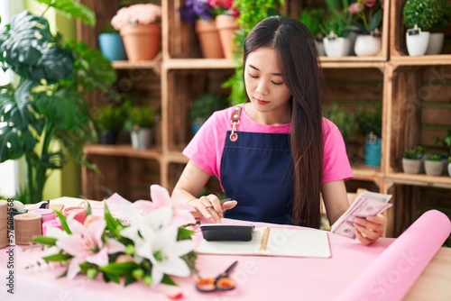 Tableau sur toile Young chinese woman florist counting dollars at flower shop