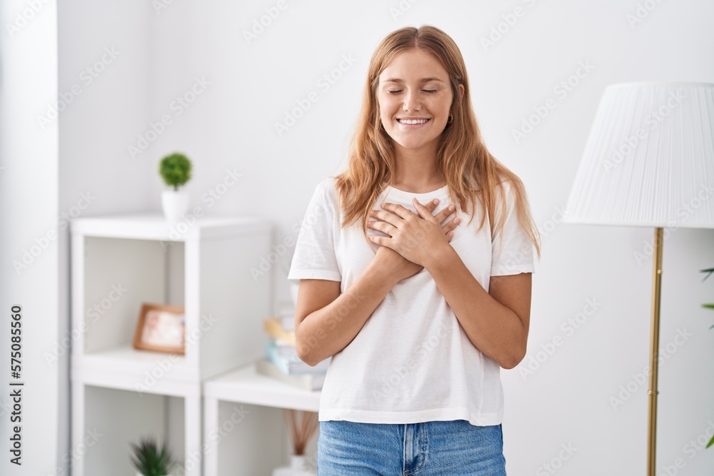 Young blonde girl standing with hands on heart at home Young blonde girl standing with hands on heart at home