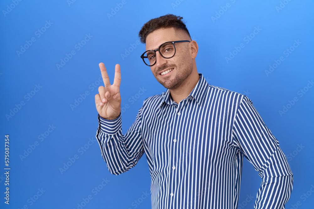Hispanic man with beard wearing glasses smiling looking to the camera showing fingers doing victory sign. number two. Hispanic man with beard wearing glasses smiling looking to the camera showing fingers doing victory sign. number two.