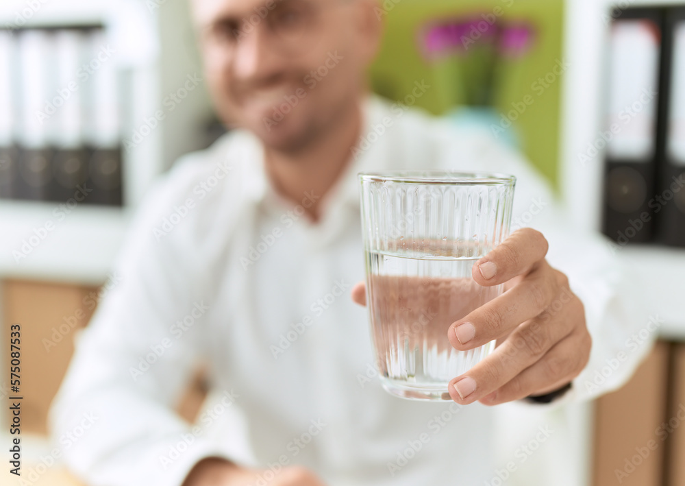 Young hispanic man business worker holding glass of water at office