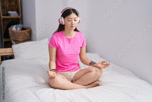 Chinese woman doing yoga exercise sitting on bed at bedroom
