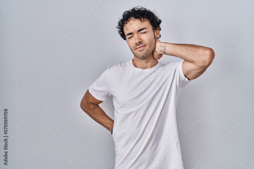 Hispanic man standing over isolated background suffering of neck ache injury, touching neck with hand, muscular pain Hispanic man standing over isolated background suffering of neck ache injury, touching neck with hand, muscular pain