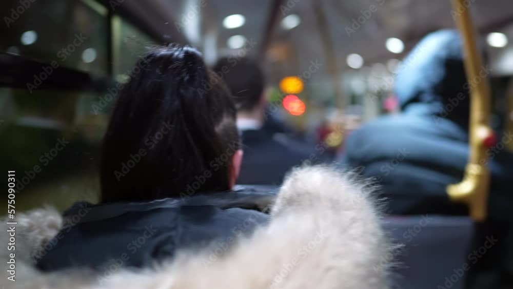 Back of female passenger commuting inside bus transportation at night. Woman wearing coat riding vehicle in motion in transit. Commuter person Back of female passenger commuting inside bus transportation at night. Woman wearing coat riding vehicle in motion in transit. Commuter person