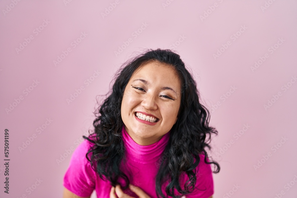 Young asian woman standing over pink background smiling and laughing hard out loud because funny crazy joke with hands on body.
