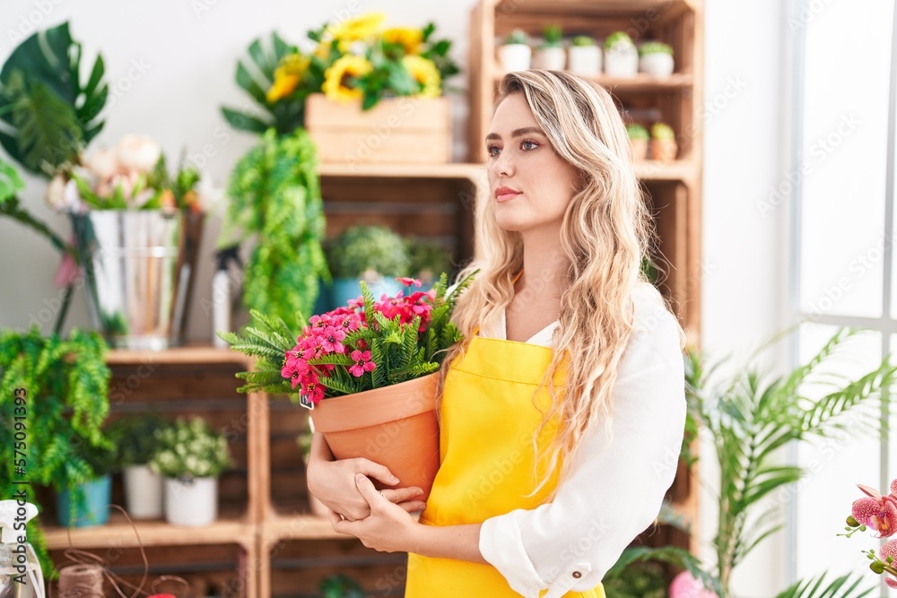 Young blonde woman florist holding plant at florist