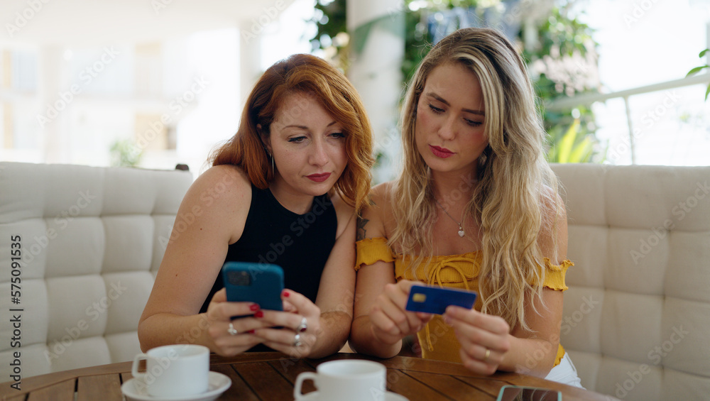 Two women using smartphone and credit card sitting on table at home terrace Two women using smartphone and credit card sitting on table at home terrace