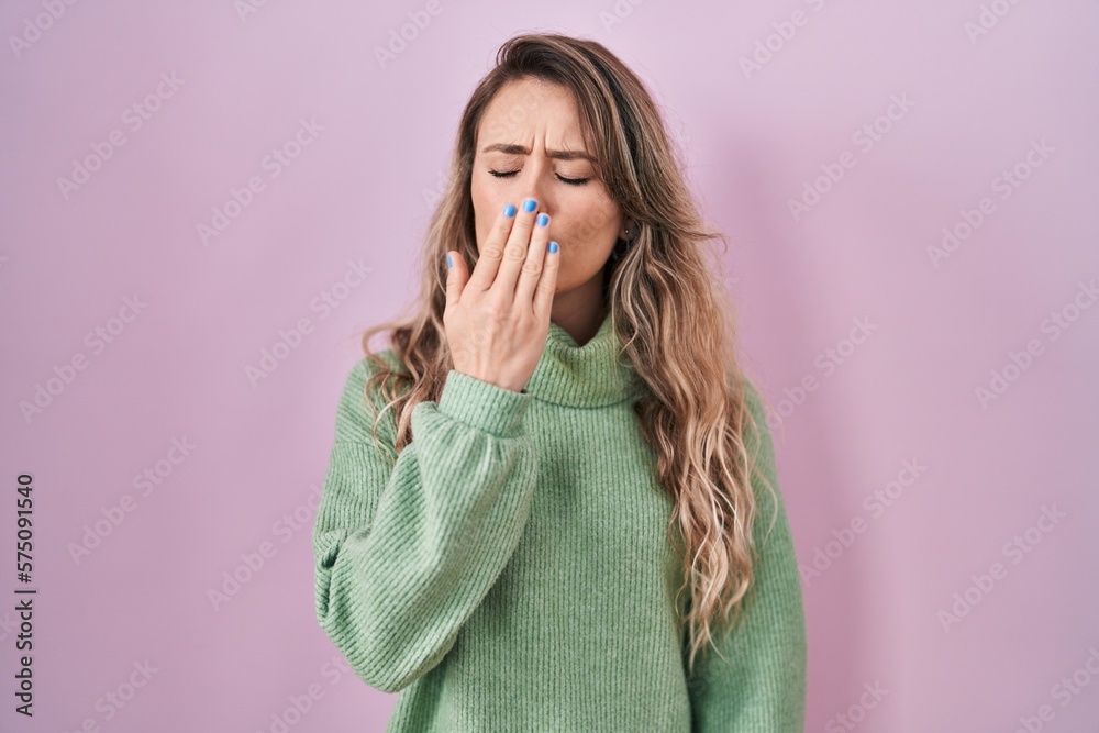Young caucasian woman standing over pink background bored yawning tired covering mouth with hand. restless and sleepiness. Young caucasian woman standing over pink background bored yawning tired covering mouth with hand. restless and sleepiness.
