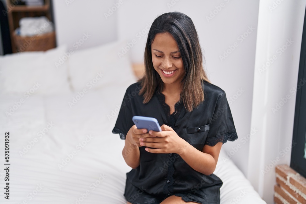 Young hispanic woman using smartphone sitting on bed at bedroom Young hispanic woman using smartphone sitting on bed at bedroom