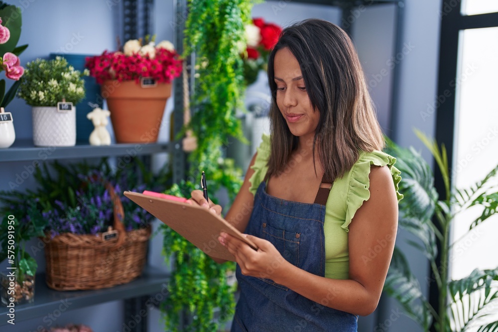 Young hispanic woman florist writing on document organize shelving at florist store Young hispanic woman florist writing on document organize shelving at florist store