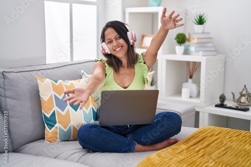 Hispanic young woman using laptop at home looking at the camera smiling with open arms for hug. cheerful expression embracing happiness.