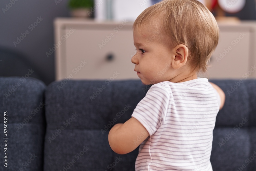 Adorable toddler standing on sofa with relaxed expression at home