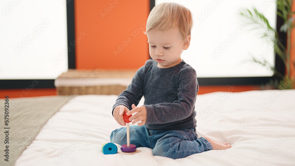 Adorable blond toddler playing with hoops toy sitting on bed at bedroom Adorable blond toddler playing with hoops toy sitting on bed at bedroom