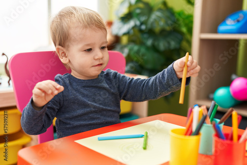 Adorable blond toddler preschool student sitting on table drawing on paper at kindergarten