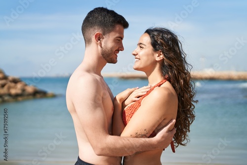 Young hispanic couple tourists wearing swimsuit hugging each other at seaside