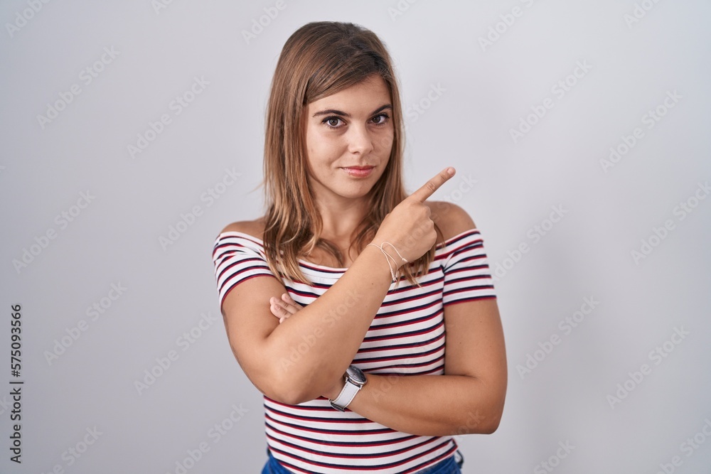 Young hispanic woman standing over isolated background pointing with hand finger to the side showing advertisement, serious and calm face Young hispanic woman standing over isolated background pointing with hand finger to the side showing advertisement, serious and calm face