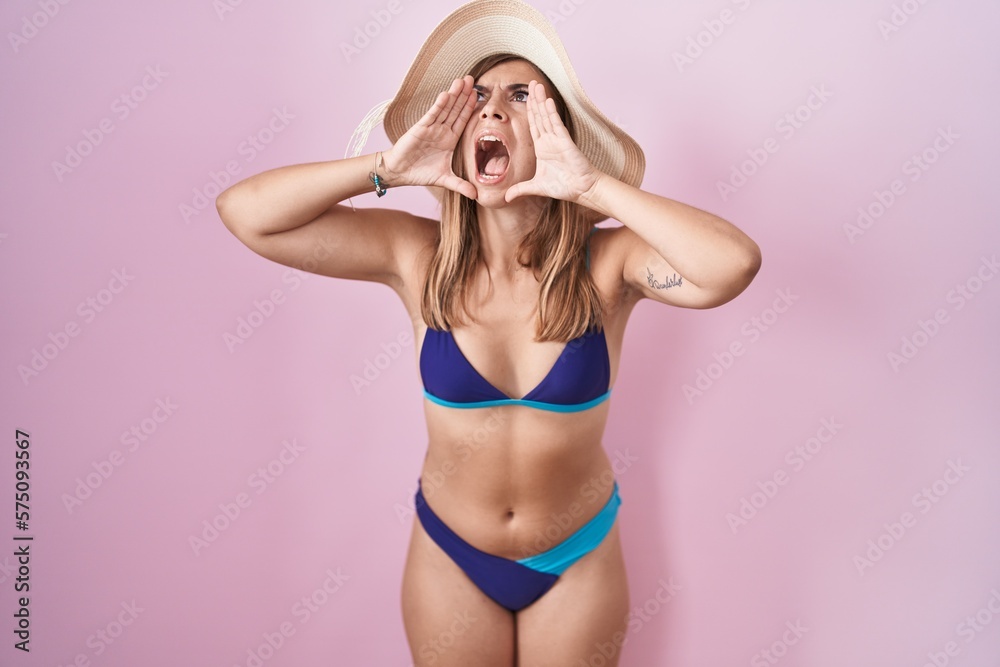 Young hispanic woman wearing bikini over pink background shouting angry out loud with hands over mouth Young hispanic woman wearing bikini over pink background shouting angry out loud with hands over mouth